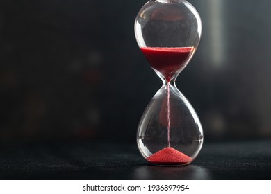 Sand passes through hourglass bulbs measuring the transit time counting down to the deadline, against a dark background