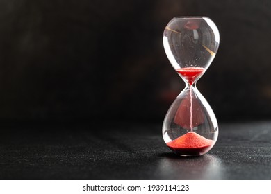 Sand passes through hourglass bulbs measuring the transit time counting down to the deadline, against a dark background