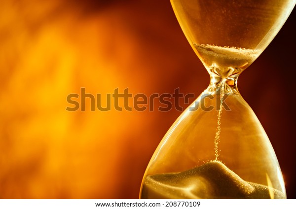 Sand passing through the glass\
bulbs of an hourglass measuring the passing time as it counts down\
to a deadline or closure on a yellow background with\
copyspace