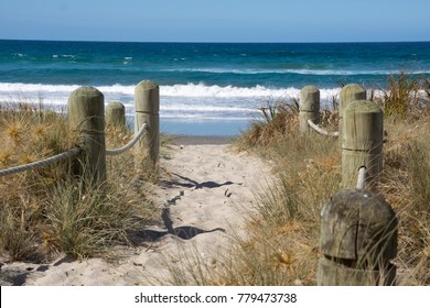 Sand pathway, edged with wooden bollards and beach vegetation, to the Mount main beach, Tauranga, New Zealand.