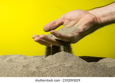 Sand Pours Through Fingers On A Yellow Background. The Concept Of Quickly Passing Time.