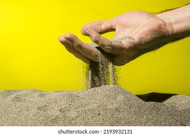 Sand Pours Through Fingers On A Yellow Background. The Concept Of Quickly Passing Time.