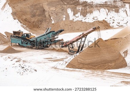 Sand quarry processing in winter with conveyor screening machinery forming aggregate stockpiles, industrial material handling in snowy excavation site