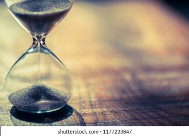 Sand Running Through The Bulbs Of An Hourglass Measuring The Passing Time In A Countdown To A Deadline, On A Dark Background With Copy Space.