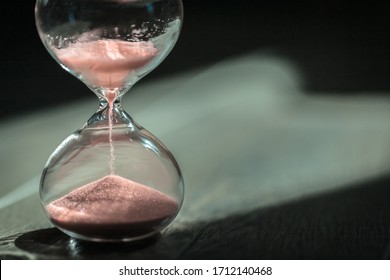 Sand running through the bulbs of an hourglass measuring the passing time in a countdown to a deadline, on a wooden floor background with copy space.