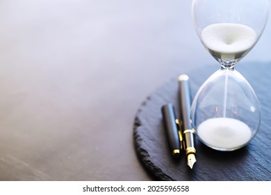 Sand Running Through The Bulbs Of An Hourglass Measuring The Passing Time In A Countdown To A Deadline, On A Dark Floor Background With Copy Space.