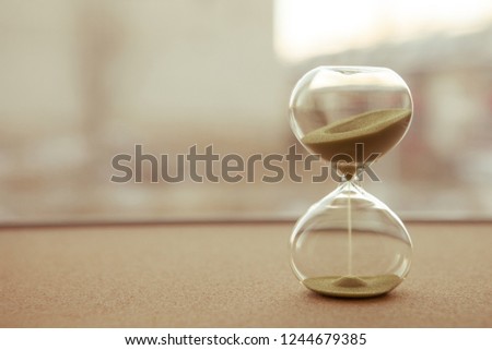 Sand running through the bulbs of an hourglass measuring the passing time in a countdown to a deadline, on a blur background