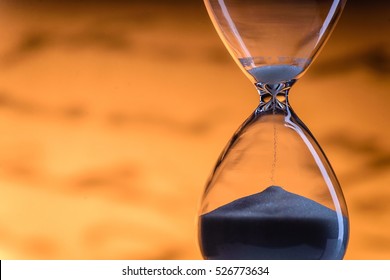 Sand running through an hourglass measuring passing time counting down towards a deadline, close up view of the glass bulbs with a blurred written document behind and copy space