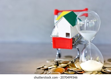 Sand Running Through The Shape Of Hour Glass, Miniature House And Shopping Cart Models With Coin Spilling On Table. Countdown Timer For Business Deadline Concept.