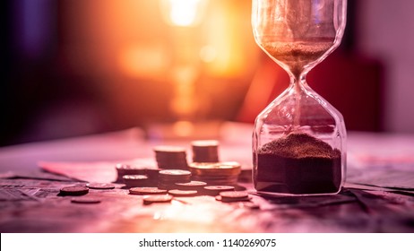 Sand running through the shape of hourglass on table with banknotes and coins of international currency. Time investment and retirement saving. Urgency countdown timer for business deadline concept - Shutterstock ID 1140269075