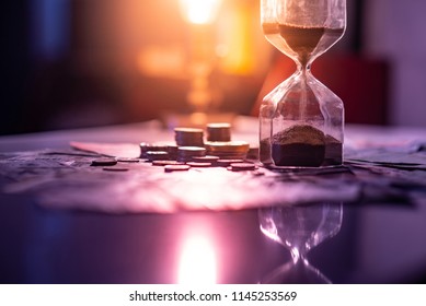 Sand running through the shape of hourglass on table with banknotes and coins of international currency. Time investment and retirement saving. Urgency countdown timer for business deadline concept