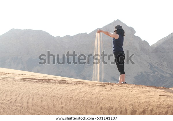 Sand slips through\
her fingers. Girl holding sand with desert dune, mountain\
background. Concept of vacation in warmer climes, the trip to the\
desert. United Arab\
Emirates.\
