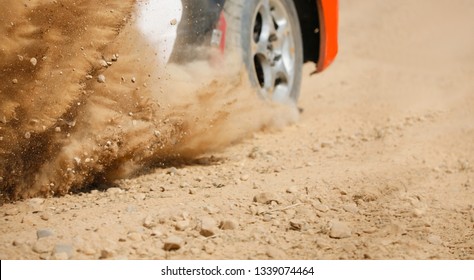 Sand splashing from rally racing car on dirt track.