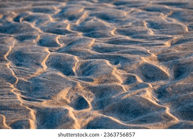 Sand structures with irregular ripples at low tide on the beach of Juist island, Germany in National Park “Wattenmeer“. Natural background pattern formed by water current and wind, selective focus.