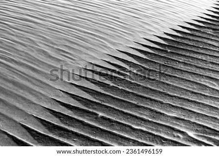 Sand structures with ripples at low tide on the beach of Juist island, Germany in National Park “Wattenmeer“. Black and white natural background pattern formed by water current with diagonal lines.