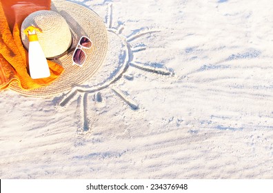 Sand Texture (background) With Hat, Towel, Sunscreen (suncream), Sunglasses On The Beach. The Sun Drawing In The Sand. The Empty Pattern For  Message. Summer Vacations Concept. Copy Space. 