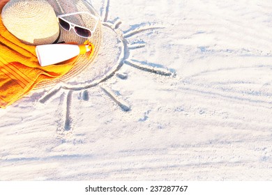 Sand Texture (background) With Hat, Towel, Sunscreen (suntan Lotion, Suncream), Sunglasses On The A Beach. The Sun Drawing In The Sand. The Empty Pattern For Message. Summer Vacations. Copy Space. 