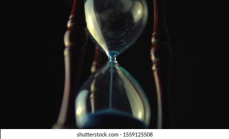 Sand timer clock with sand flowing countdown from through hour glass. View from below hourglass close up macro shot. Black background.