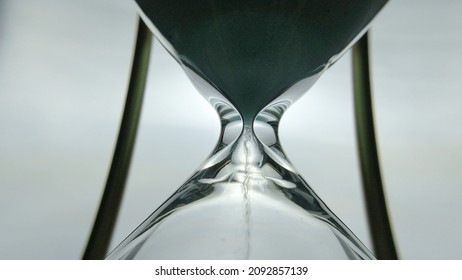 Sand timer clock with sand flowing countdown from through hour glass. View from below hourglass close up macro shot. White background.