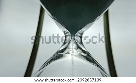 Sand timer clock with sand flowing countdown from through hour glass. View from below hourglass close up macro shot. White background.