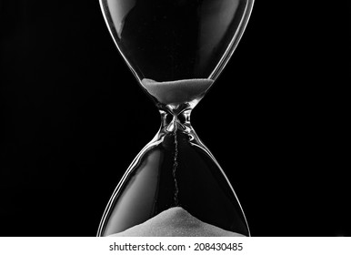 Sand Trickling Through The Bulbs Of An Hourglass Or Egg Timer Measuring The Passage Of Time On A Dark Background