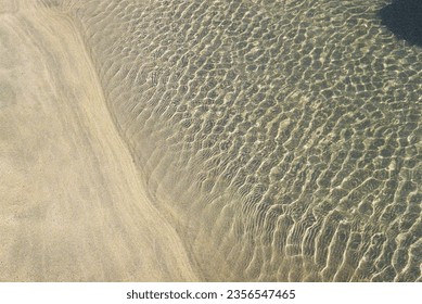 Sand, water and wind meet in this photo with ripples casting shapes and shadows on the waters edge. Taken on an Asahi Pentax camera on the beaches of Cornwall, UK.
