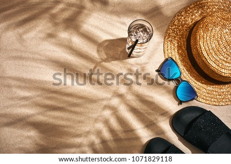 Sandal, straw hat and sunglasses on a sandy background, top view