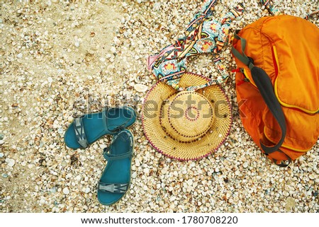 Sandal, straw hat, swimwear and orange bag on seashells background, top view. Female beach accessories for summer beach vacation