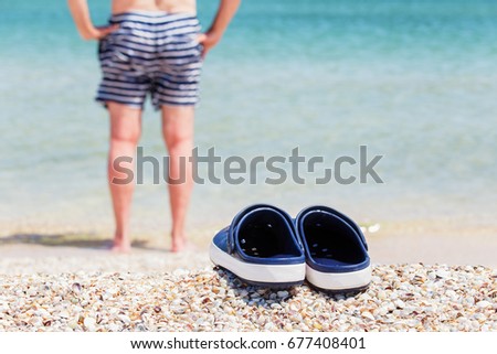 Sandals, clogs on the shell seaside. Against a background, a person in swimming trunks goes into the water.