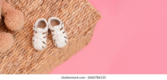 Sandals shoes for a child on a wicker basket on a pink background, the concept of childhood and newborns