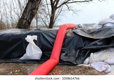 Sandbag Flood Protection Covered With Black Nylon And Held With New Sandbags Next To Large Water Pump Hose