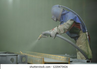 Sandblast. An employee prepares a metal part for painting. A harsh man works in the factory. A man in a protective form. Sparks fly
