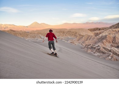 Sandboarding during sunset in Atacama desert, chile. A guy on a snowboard riding down a dune. Sandboarding in the 'Valle de la Luna', the valley of the Moon in Atacama desert, Chile. Guy in red shirt. - Powered by Shutterstock