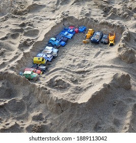 Sandcastle With Kids Toys. Sand Castle Or Fort With Many Colorful Plastic Car On Summer Sea Coast Overhead View. Abstract Background.