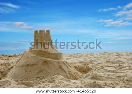 A sandcastle on a sandy beach, set against a bright blue summer sky.