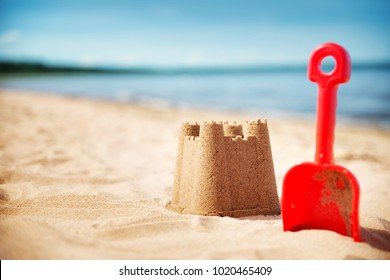 Sandcastle with a shovel on the sea in summertime. Seashore on beautiful day. Sand on the beach and blue water