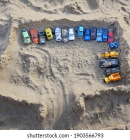 Sandcastle Top View On Sea Beach With Kids Toys. Sand Castle Or Fort With Many Colorful Plastic Car On Summer Sea Coast Overhead View. Abstract Background.