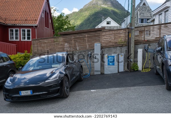 Sandeid, Norway - June\
7, 2022: A static shot of a solid black Tesla Model 3 dual motor\
charging at the Haugaland Kraft AC charging station in a rainy\
spring day. Selective\
focus.