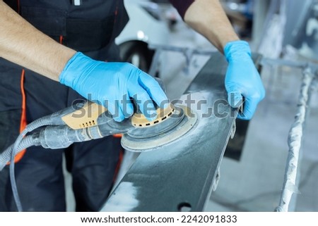 Sanding a car body part with electrical grinder machine before painting, vehicle body repair service