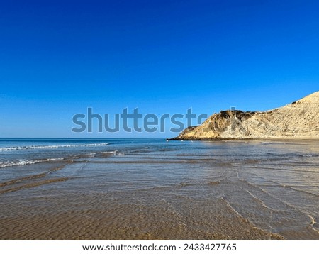 Sandstone hill reflection at the wet shore, sandy ocean coast, natural colors, clear blue sky, calm water 