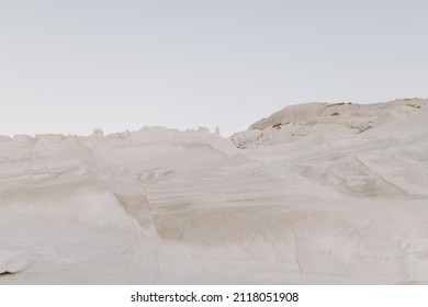 The sandstone white rocks cliffs moonscape of Sarakiniko volcanic beach in Milos Island in Greece surrounded by turquoise blue waves and sea at sunset