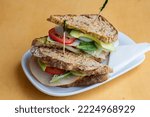 A sandwhich on a white plate with a yellow background.