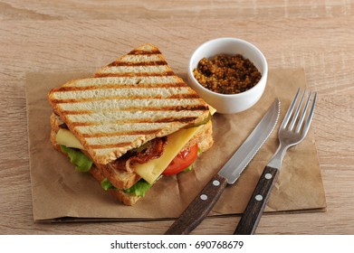 Sandwich With Bacon, Cheese, Tomato And Dijon Mustard With Cutlery On A Paper Towel