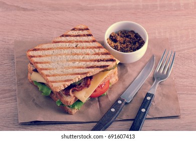 Sandwich With Bacon, Cheese, Tomato And Dijon Mustard With Cutlery On A Paper Towel In Vinage Aged Style