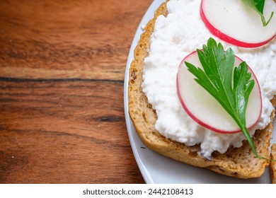 Sandwich with black bread, cottage cheese, radishes and parsley on white plate and wooden board - Powered by Shutterstock