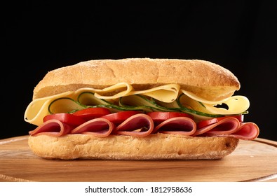 Sandwich With Ciabatta Bun, Thin Slices Of Sausage And Edam Cheese On Brown Wooden Board, Black Background