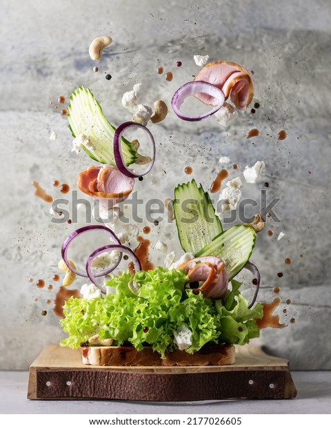 Sandwich with flying ingredients on wooden\
board on textured background. Levitation healthy food creative\
concept. Vertical\
orientation
