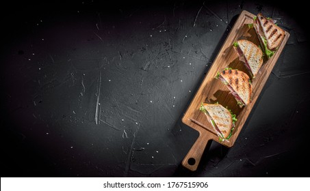 Sandwich With Ham, Cheese, Tomatoes, Lettuce, And Toasted Bread On Dark Background. Top View With Copy Space