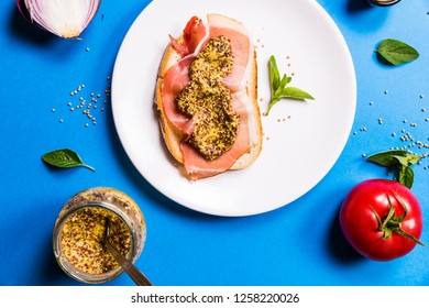 Sandwich With Ham And Mustard On A White Ceramic Plate, Blue Backgrounds With Ingredients, Top View