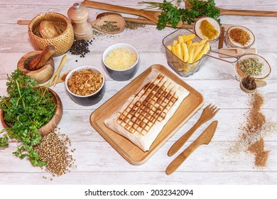 Sandwich Kebab taco with french fries, onions and cheese, in a fast food restaurant, served on a wooden board with food decoration in background with vegetables.